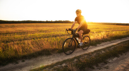 Obraz premium Bike traveler riding through the field at sunset on bicycle with bags