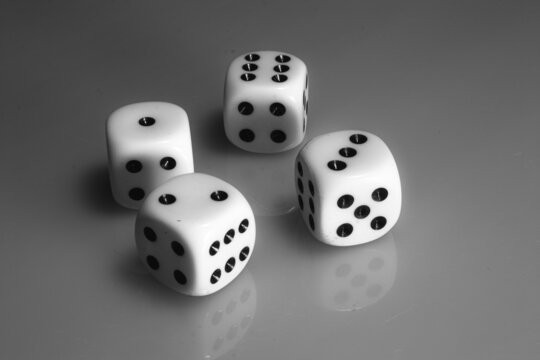 Black and white photo of four white dices for gambling on a matt reflective surface