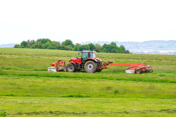 A red tractor mows the grass with two mowers. Harvesting hay for cows for the winter.