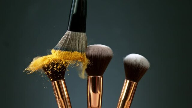 Makeup brushes touch each other on dark background and small particles of cosmetics, super slow motion, 1000 fps.