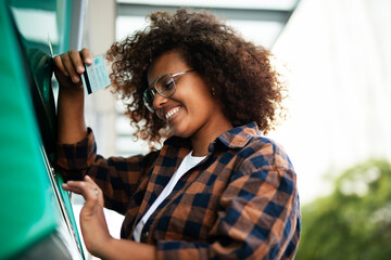 Beautiful African girl using ATM machine. Happy smiling young woman withdrawing money from credit...