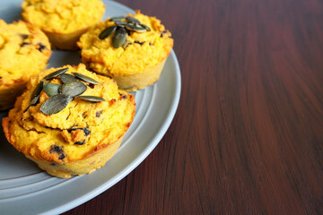 place a few pumpkin muffins without gluten and sugar, sprinkled with pumpkin seeds, on a gray plate on a wooden table next to it . side view