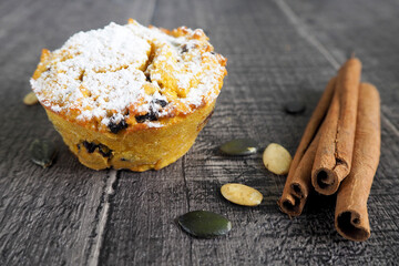 a gluten-free pumpkin muffin, sprinkled with powdered sugar, lies on a wooden table next to cinnamon sticks on the table . side view