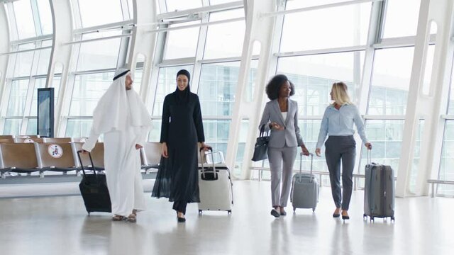 Full length view of the diverse business team of the co-workers walking the airport with suitcases on wheels and talking while traveling on the working trip