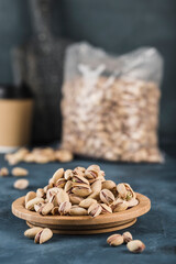 Pistachios on a wooden plate and in a package with a coffee cup on a dark blue background.