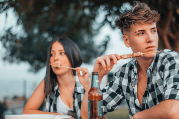 Muchacha joven y hombre comiendo pinchitos de pollo en un picnic al aire libre con amigos junto con...