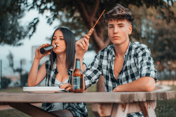 Cita romántica de adolescentes jóvenes en un parque al aire libre bebiendo cerveza y comiendo