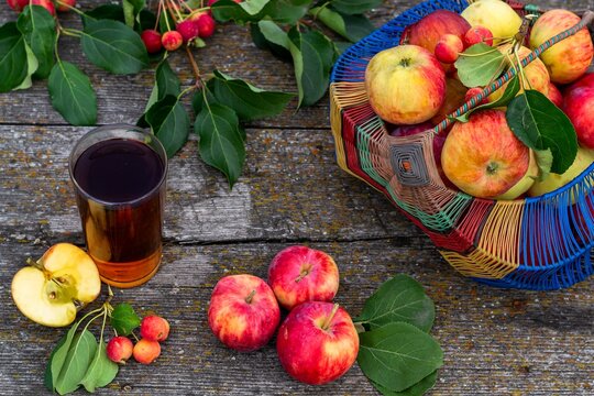 Summer still life in a rustic style, ripe garden apples in a basket and lie on the table, a glass of apple juice. Horizontal photo close-up