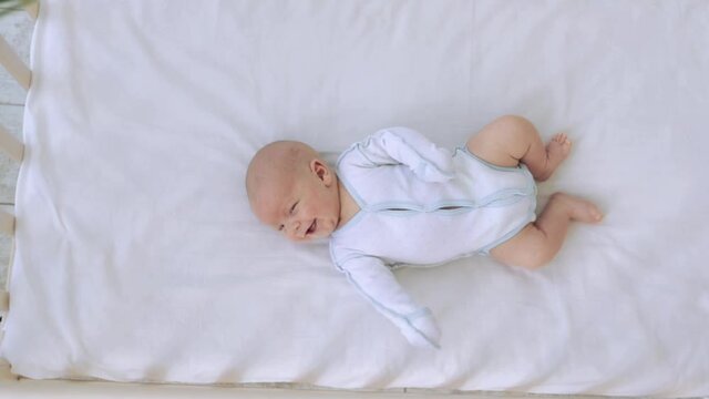 small newborn baby boy smiles in a cot on a cotton bed, healthy baby sleep concept