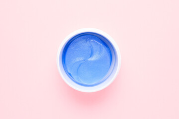 Blue cosmetic hydrogel eye patches in a white plastic jar on a pink background. Place for text. Skin care under the eyes. Top view.
