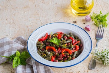 Warm salad or vegetable stew made from asparagus beans, canned red beans and roasted red bell peppers in a white plate on a light concrete background. Beans recipes. Vegan food.