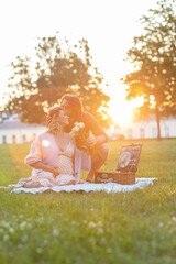 Beautiful pregnant young couple having a picnic at sunset