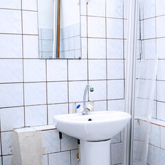 Bathroom interior with a white sink and faucet on the background of a mirror and a tiled wall