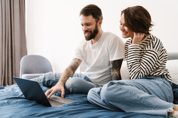 Portrait of smiling young white couple and using laptop while lying in bed at home