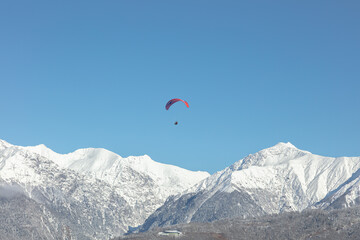 the red wing of the paraglider against the background of the blue sky and the snow-white peaks of the high mountains. the parachutist during the flight against the background of the Alpine mountains