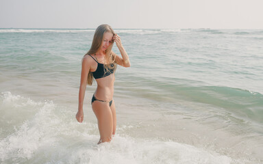 beautiful young smiling caucasian girl in swimsuit bikini standing in white sand tropical beach