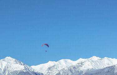 the red wing of the paraglider against the background of the blue sky and the snow-white peaks of...