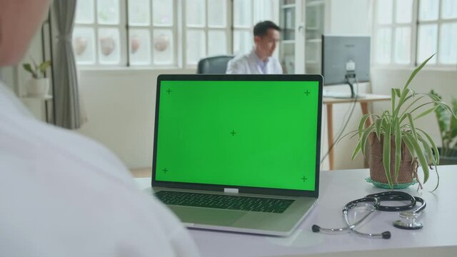 Close Up Asian Woman Doctor Is Using Laptop Computer With Mock Up Green Screen Display In Workplace. Medical Concept
