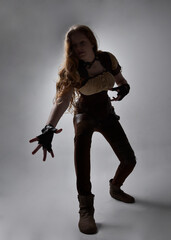 Full length portrait of beautiful young woman with long red hair, wearing steampunk inspired costume. Standing action pose isolated on studio background.