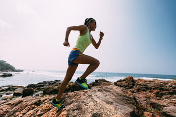 Young fitness woman trail runner running to rocky mountain top on seaside