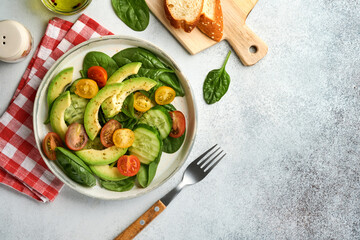 Avocado, red, yellow, black cherry tomato, spinach and cucumber fresh salad with spices pepper and olive oil in grey bowl on grey slate, stone or concrete background. Healthy food concept. Top view.