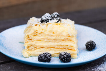 puff cake with blackberries on a blue plate on a wooden background
