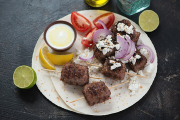 Roasted greek kofta served with feta, white yogurt and tomatoes on a flatbread, studio shot on a dark brown stone surface