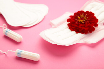 Menstrual tampons and pads on pink background. Menstruation cycle. Hygiene and protection. A rose flower lies on a menstrual pad.