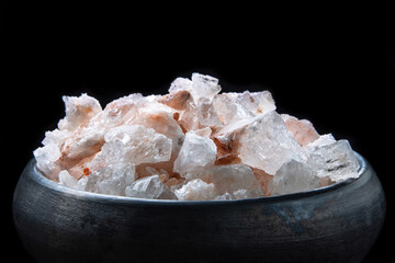 Large chunks of pink himalayan salt in black handmade earthenware bowl isolated on black background