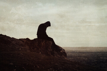 A mental health concept of a sad lonely hooded figure sitting on top of a hill. With a grunge, textured edit