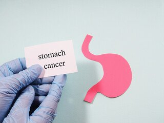 A hand in a medical glove holds a sign with the inscription stomach cancer on the background of the silhouette of the stomach