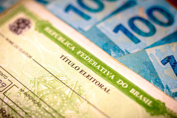 Obraz premium In this photo illustration the Voter License (Título Eleitoral). Photo election vote card (voter id). One hundred reais bills in the background.