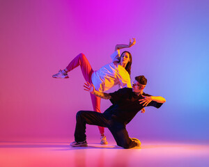 Two young people, guy and girl in casual clothes dancing contemporary dance, hip-hop over pink...