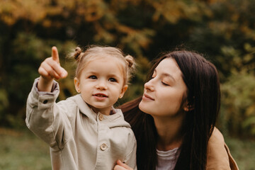 Young happy and smiling mom with her little daughter in arms hugging and kissing spending a weekend...