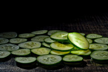 Pieces of cucumber on a pile close up. Cucumber slices on a black background. Contrasting dramatic light as an artistic effect.