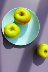 three green fresh apples on a blue plate