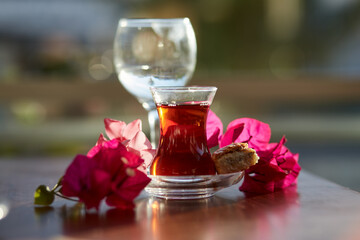 Turkish delight and traditional glass of turkish tea with bougainvillea flowers. Romantic dinner concept. Relaxing, calming drink Travel Turkey concept. Bright relaxing drink