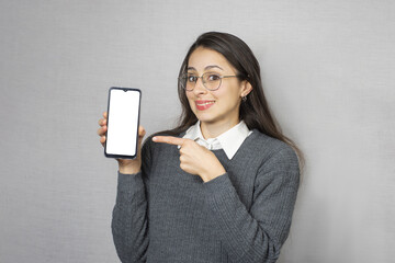 Mujer feliz con sonrisa sosteniendo y señalando celular. Fondo blanco