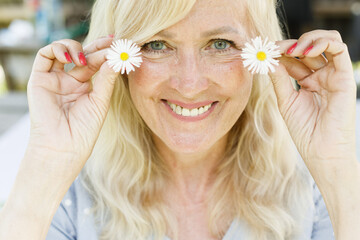 Portrait of smiling mature woman with flowers. Natural skin care. Female and white daisies. Organic and healthy lifestyle. Natural make up. Beauty of aging. Facial caring