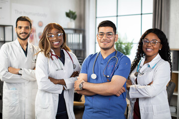 Portrait of smiling multiethnic medical team standing in modern clinic room with arms crossed. Group of pleasant confident skilled multiracial physicians posing indoors with arms folded