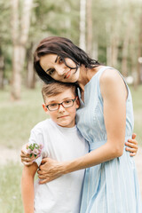 A young beautiful mother hugs her little son during the sunset in nature. Happy family walk in the park.