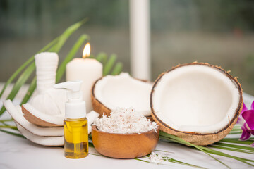 Coconut oil, tropical leaves and fresh coconuts. Spa coconut products on light wooden background. Spa still life of organic cosmetics with coconuts on a light wooden background, body care concept.