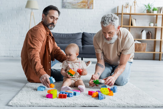 Homosexual parents playing building blocks with daughter on carpet