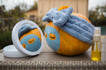 large orange pumpkin with painted eyes, lips and a clay mask in front of a round mirror during a...