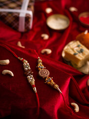 Raksha Bandhan background with an elegant Rakhi and Rice Grains on red cloth textured background.