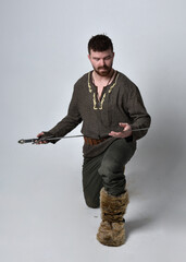 Full length  portrait of  young handsome man  wearing  medieval Celtic adventurer costume.  Standing pose holding a sword, isolated on studio background.