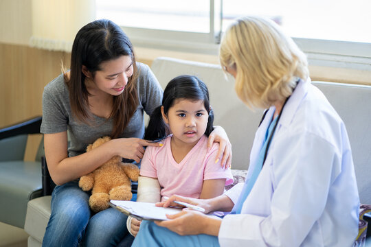 Pediatrician doctor examining little asian girl with a broken arm wearing a cast at hospital