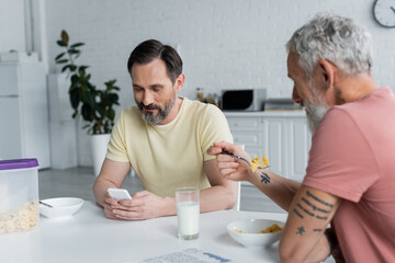 Same sex couple using smartphone during breakfast in kitchen