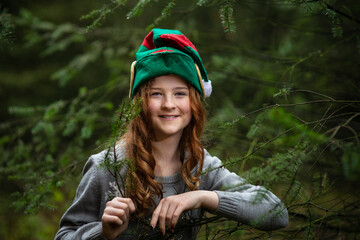 Weihnachten. ein Mädchen mit langen Haaren sieht aus wie ein Wichtel. Sie hat eine grüne Wichtelmütze auf  dem Kopf. Wichtel steht im Wald. 