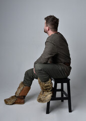 Full length  portrait of  young handsome man  wearing  medieval Celtic adventurer costume.  Sitting pose, isolated on studio background.